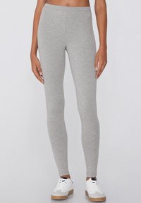 Leggings gris fabriqués en tissu doux, au design ajusté et de longueur complète. Associés à des baskets blanches avec une semelle texturée.