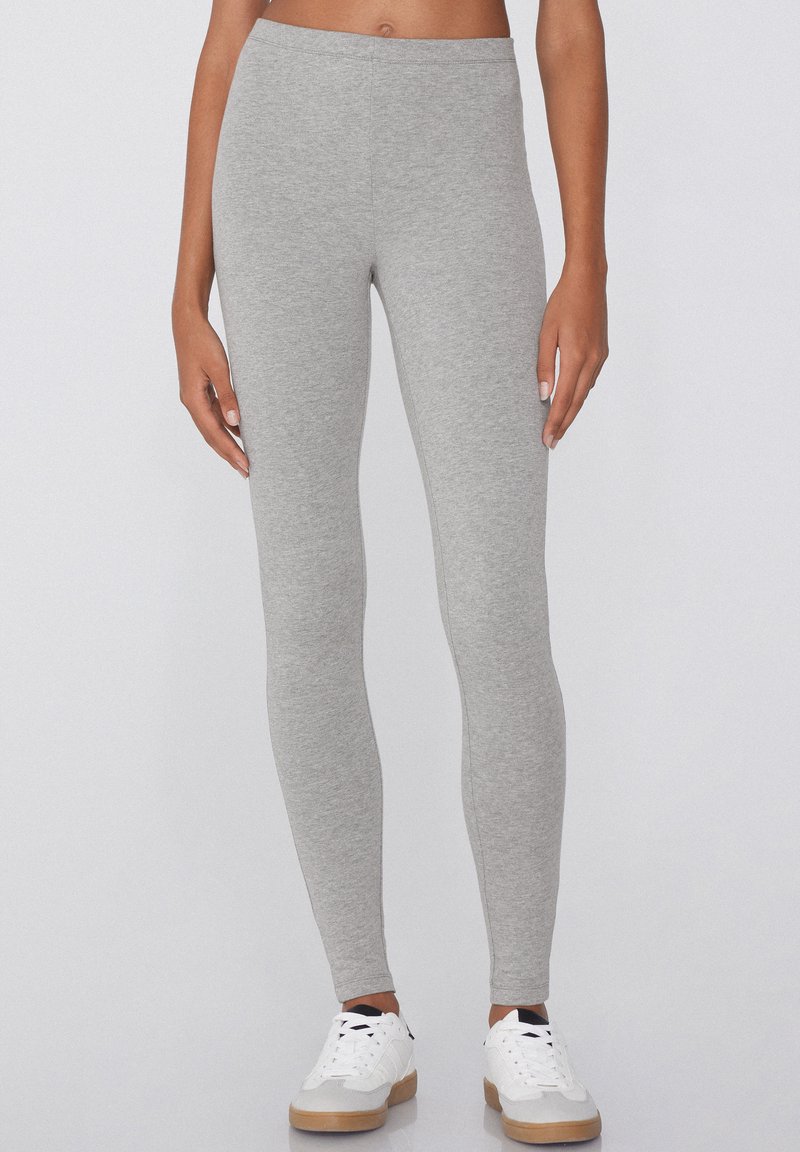 Leggings gris fabriqués en tissu doux, au design ajusté et de longueur complète. Associés à des baskets blanches avec une semelle texturée.