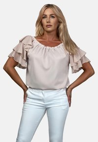 Jasnoróżowa bluzka z falbankowymi rękawami, okrągłym dekoltem i miękkiego materiału. Połączona z białymi dopasowanymi spodniami dla minimalistycznego wyglądu.