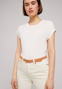 Camiseta blanca de manga corta combinada con jeans de color claro y un cinturón marrón claro con una hebilla de metal. Tejido suave y diseño sencillo.