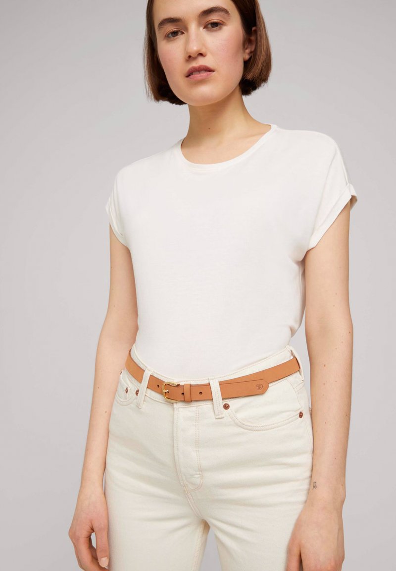 Camiseta blanca de manga corta combinada con jeans de color claro y un cinturón marrón claro con una hebilla de metal. Tejido suave y diseño sencillo.