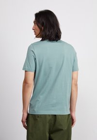 Tricou scurt cu mânecă scurtă, de culoare albastru deschis, realizat dintr-un material moale, cu guler rotund și o croială lejeră, asociat cu pantaloni de culoare verde măsliniu.