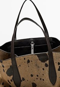 Borsa tote in pelle marrone e nera con macchie, dotata di due manici in pelle scura, che presenta un design elegante e strutturato e un ampio interno aperto.