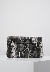 Bolso de mano con estampado de serpiente en blanco y negro, de forma rectangular estructurada, con una solapa plegable y una cadena como asa para el hombro.