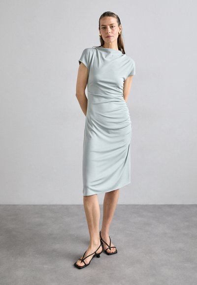 Vestido verde claro, hasta la rodilla, con un diseño drapeado y mangas cortas, hecho de una tela suave. Corte minimalista con sutiles detalles de fruncido.