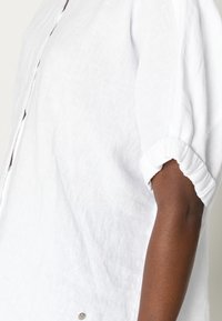 Vit linnetopp med puffärmar, samlade manschetter och knappstängning. Har ett texturerat tyg och en avslappnad passform.