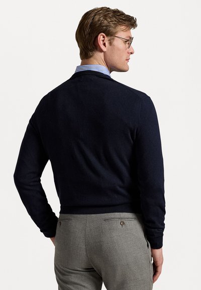 Jersey de punto en navy con cuello redondo y dobladillo acanalado, combinado con pantalones de corte recto en gris claro que cuentan con bolsillos traseros y botones.