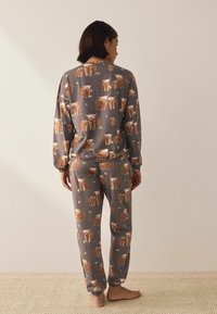 Graues Pyjama-Set mit einem großflächigen Druck brauner Hochlandrinder, mit elastischen Bündchen an Ärmeln und Beinen, hergestellt aus weichem Stoff.