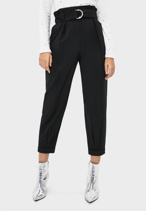 Un pantalon noir taille haute avec une taille ceinturée, un devant plissé, une jambe fuselée et des ourlets roulés, assorti à des bottines argentées brillantes.
