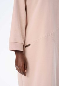 Langärmliges, hellrosa Kleid aus weichem Stoff. Verfügt über ein strukturiertes Detail und ein kleines, metallisches Logo-Tag nahe dem Saum.