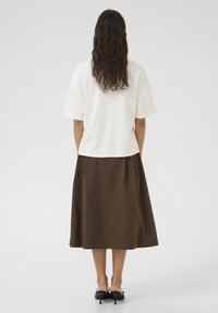 Valge lühikeste varrukatega tipp, millele on sobitatud pruun midi-seelik. Tipp on mugava lõikega, samas kui seelikul on sile tekstuur ja voogav kuju.