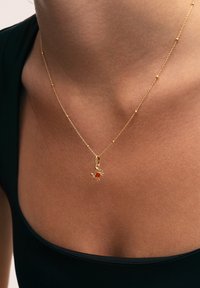 Collier en or avec un petit pendentif en forme de crabe, mettant en avant une pierre rouge centrale, avec une surface lisse et des accents délicats de perles le long de la chaîne.