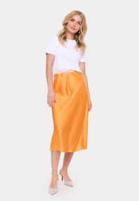 Oranje satijnen midi rok met een gladde textuur en een elastische tailleband, gecombineerd met een eenvoudige witte t-shirt en versierde hakken.