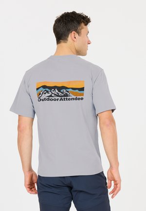 Mann trägt ein graues T-Shirt mit einem Bergmotiv und dem Schriftzug "Outdoor Attendee" auf der Rückseite, kombiniert mit dunkelblauen Shorts.