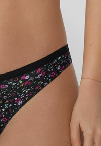 Culotte de bikini noire à imprimé floral avec une taille élastique douce. Présente de petites fleurs multicolores sur un fond sombre. Texture lisse.