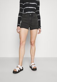 Mustat farkkushortsit revityllä helmalla, yhdistettyinä valkoisiin nauhakengiin. Mallilla on päällään musta toppi, jossa on valkoista sidottua väritystä.