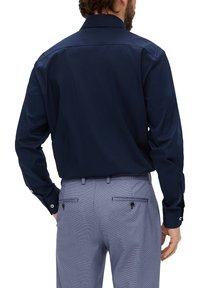 Marineblauwe langemouwen shirt met knoopmanchetten, gecombineerd met gestreepte broek met achterzakken en knoopaccenten.