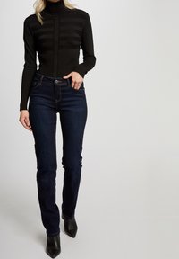 Zwarte geribbelde coltrui met horizontale strepen, gecombineerd met donkerblauwe aansluitende jeans en zwarte enkellaarsjes met een spitse neus. Strak ontwerp, geen patronen.