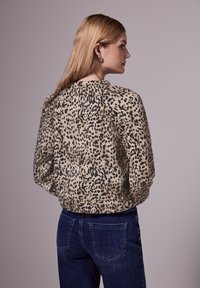 Blouse imprimé léopard en beige et noir. Tissu doux, coupe ample avec ourlet froncé. Associée à un jean bleu foncé, avec un design minimal sur les poches.
