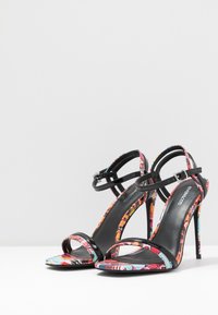 I sandali con tacco alto presentano una stampa floreale colorata con cinturini in vernice nera e una delicata fibbia alla caviglia; design open-toe con un tacco sottile.