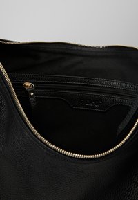 Czarna skórzana torba od środka, pokazująca otarty złoty zamek błyskawiczny i wewnętrzną kieszeń na zamek z teksturowanym podszewką.