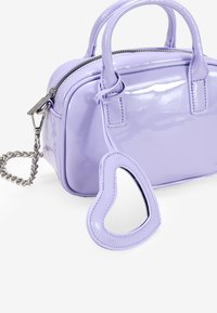 Bolso de mano de charol lila con dos asas superiores, cremallera plateada y charm en forma de corazón desmontable. Acabado compacto y brillante.