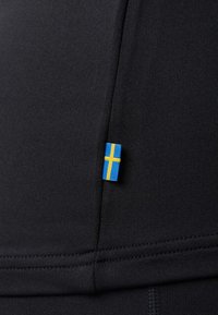 Abbigliamento sportivo in tessuto nero con un piccolo tag della bandiera svedese. Texture liscia con dettagli di cucitura visibili, che evidenziano il suo design aderente.