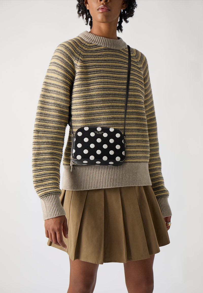 Suéter de punto a rayas en beige y amarillo, con un cuello de canalé gris; falda marrón plisada; pequeña bolsa cruzada negra con lunares.