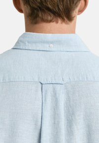 Lichtblauwe linnen overhemd met een button-down kraag, voorzien van een yoke detail en een enkele knoopsluiting aan de achterkant. Soepele textuur en casual ontwerp.