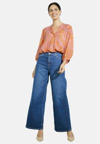 Světle růžová blůza s oranžovým květinovým vzorem, která je zkombinována s vysokým pasem a širokými modrými džíny. Outfit doplňují béžové podpatky.