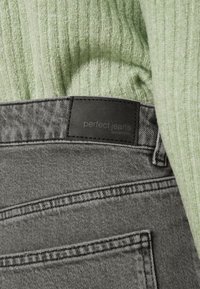 Gray jeans with a black leather label reading "perfect jeans" on the waistband, accompanied by a light green ribbed sweater.