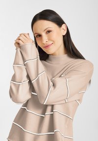 Lichtbeige trui met witte en zilveren horizontale strepen, met een hoge hals en lange mouwen. Zachte textuur, relaxte pasvorm.