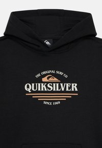Black hoodie with a kangaroo pocket, featuring a cream and light brown Quiksilver logo and "THE ORIGINAL SURF CO" text above.
