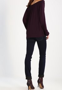 Violetti olkaamaton paita, pitkät hihat, yhdistettynä tummansinisiin slim-fit-farkkuihin ja ruskeisiin nilkkureihin, joissa on korkea korko ja vetoketjusisustus.
