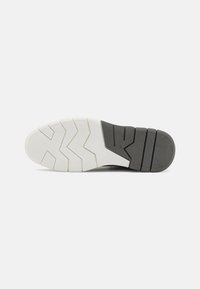 Egy sneaker talpa, amely vastag gumideszignal készült, és zigzag mintázattal rendelkezik. Színe feketéből fehérbe megy át az elülső részen.