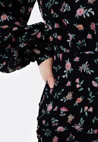 Svart blommig klänning med små mönster av rosa, gröna och gula blommor. Mjuk tyg med puffärm och fickdetalj.