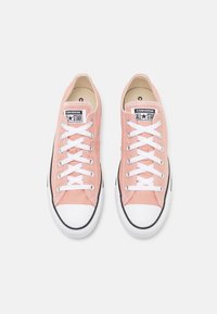 Růžové plátěné nízké tenisky s bílými tkaničkami, černou gumovou podrážkou a bílým špičkovým krytem. Obsahují logo na jazyku.