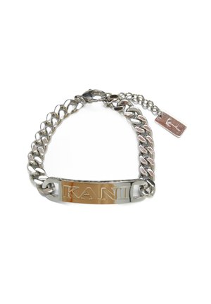 Bracelet en chaîne avec des maillons en argent poli, une plaque métallique centrale gravée de "KANI" et une petite étiquette fixée à une extrémité.