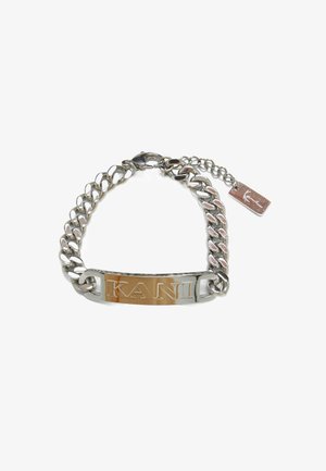 Verižica iz verige z gladkimi srebrnimi povezavami, osrednjo gravirano kovinsko ploščico z napisom "KANI" in majhno oznako, pritrjeno na enem koncu.