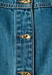 Nära bild av blå denimtyg som visar en rad med guldmetallknappar med bruna trådkantningar, vilket visar en strukturerad och hållbar yta.