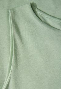 Ljusgrön ärmlös topp gjord av mjukt, texturerat tyg, med rund halsringning och rena sömmar längs kanterna.