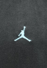 Tecido preto com um logótipo Jumpman bordado em azul claro, exibindo um jogador de basquetebol em pleno salto, com uma textura suave.