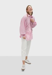 Ružićasta košulja s dugim, napučenim rukavima složena preko svijetlo ružićaste majice. Uparena s bijelim skraćenim hlačama i svijetlim tenisicama.