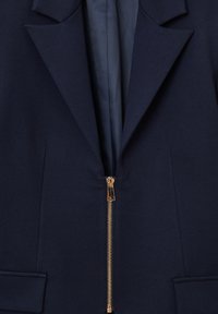 Blazer blu navy con colletto a punta, chiusura frontale con zip e due tasche laterali. Tessuto liscio con finitura opaca e forma strutturata.