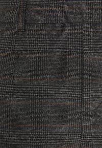 Tissu texturé noir et gris avec un motif à carreaux, présentant de fines lignes couleur rouille. Le matériau semble tissé et dense.