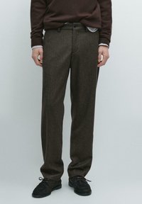 Pantaloni di lana marrone con finitura testurizzata, design a gamba dritta e tasche frontali, abbinati a scarpe nere con lacci.