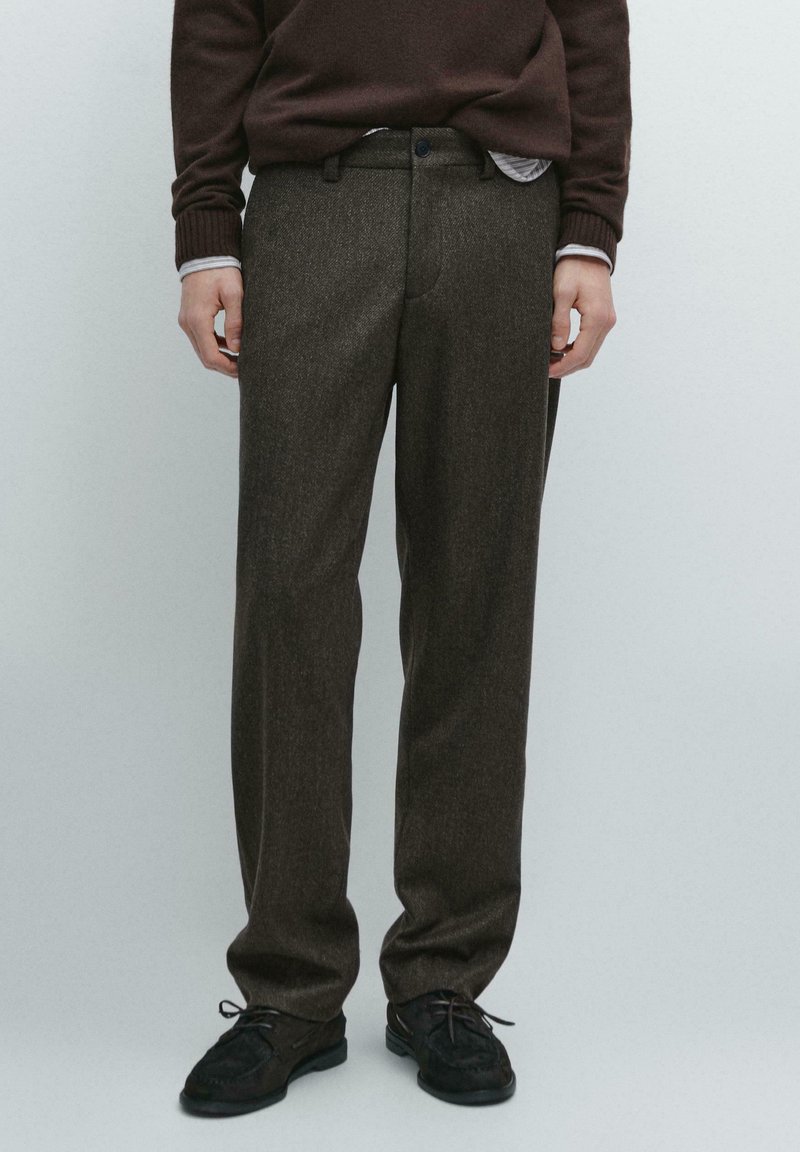 Pantaloni di lana marrone con finitura testurizzata, design a gamba dritta e tasche frontali, abbinati a scarpe nere con lacci.