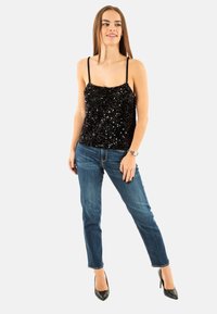 Camiseta de tirantes finos con lentejuelas negras, combinada con jeans de mezclilla azules y tacones negros de punta. Look simple y casual.