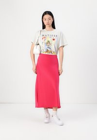 T-shirt gris avec graphisme "Matisse", jupe midi en satin rose, et baskets blanches. La tenue comprend un sac à main blanc minimaliste.