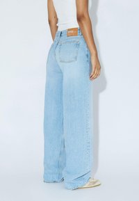 Light blue wide-leg jeans made of denim, featuring a high waist, back pockets, and a branded leather patch on the waistband.